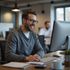 Man wearing glasses smiles while working on a computer in an office.