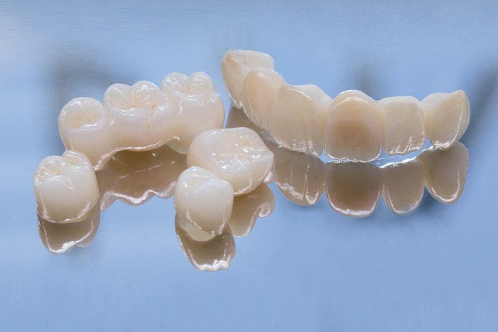 Dental crowns and bridges, white porcelain, reflected on a blue surface.
