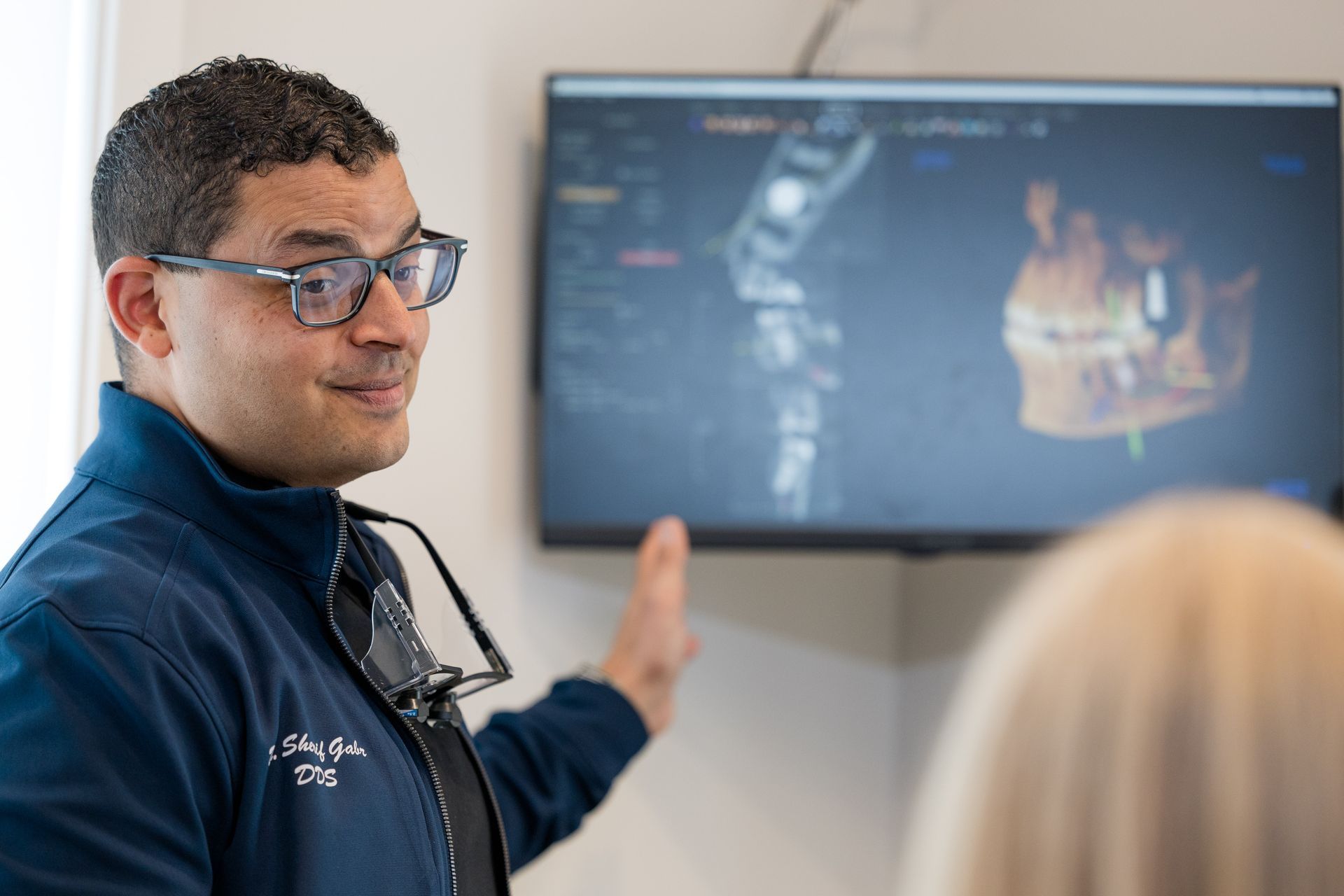 A dentist is talking to a patient in front of a computer screen.