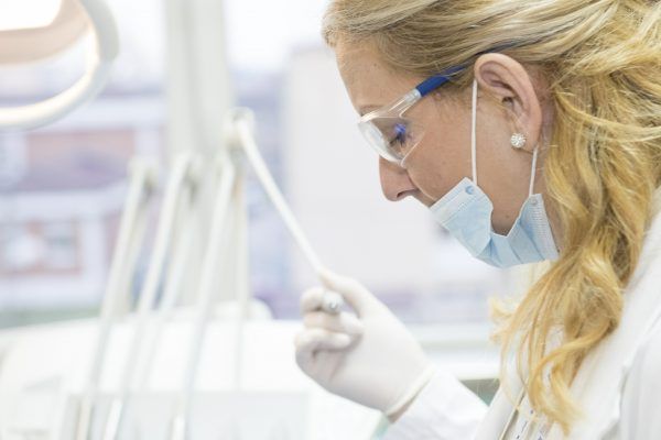 A female dentist wearing a mask and glasses is working on a patient 's teeth.