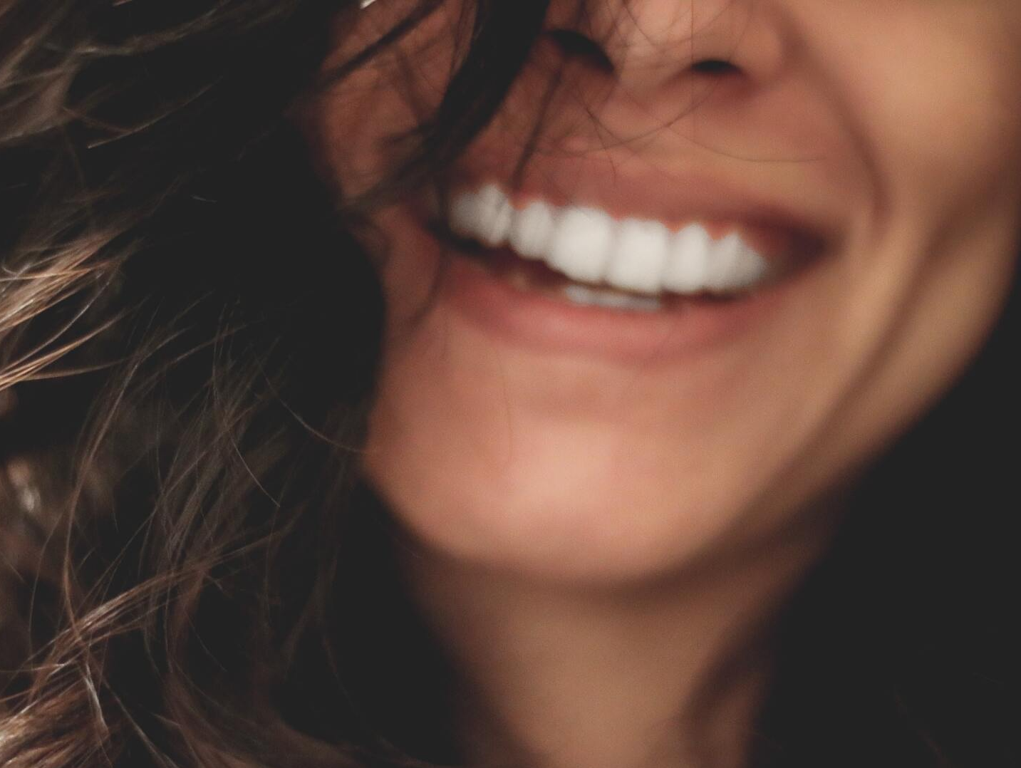 A close up of a woman 's mouth smiling with her hair blowing in the wind.