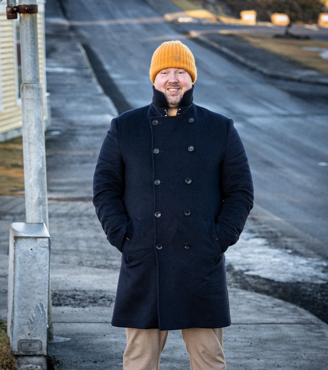 A man wearing a black coat and a yellow hat is standing on a sidewalk