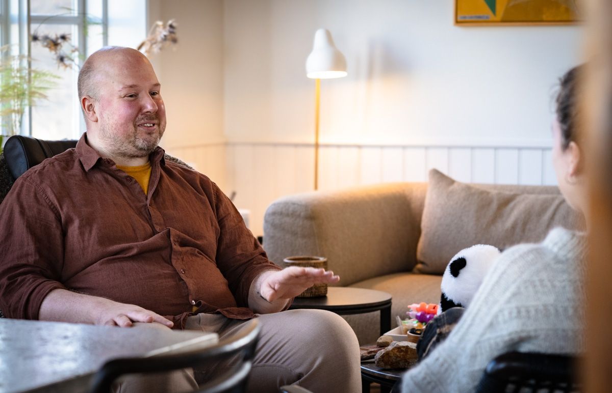 A man is sitting in a chair talking to a woman in a living room.