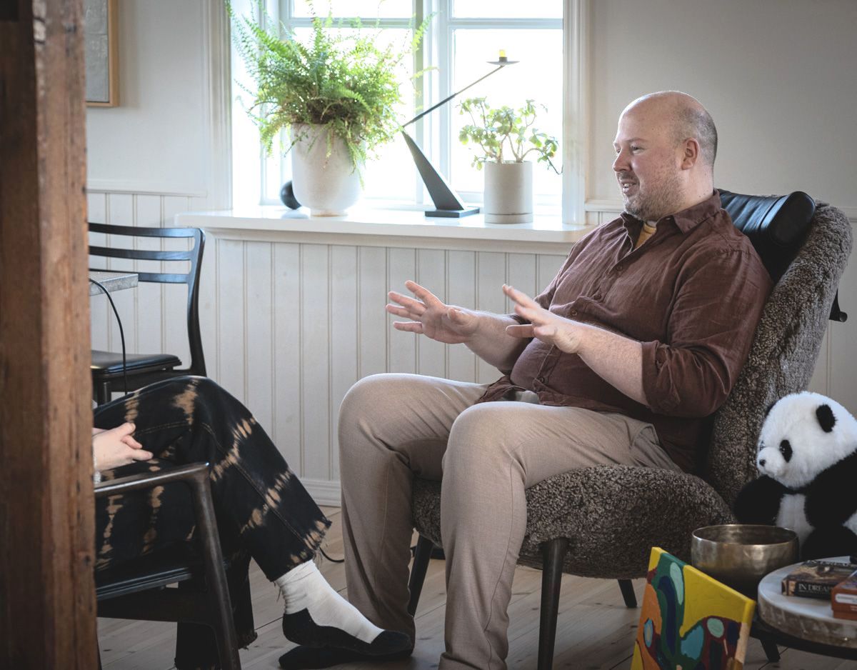 A man is sitting in a chair talking to another man.