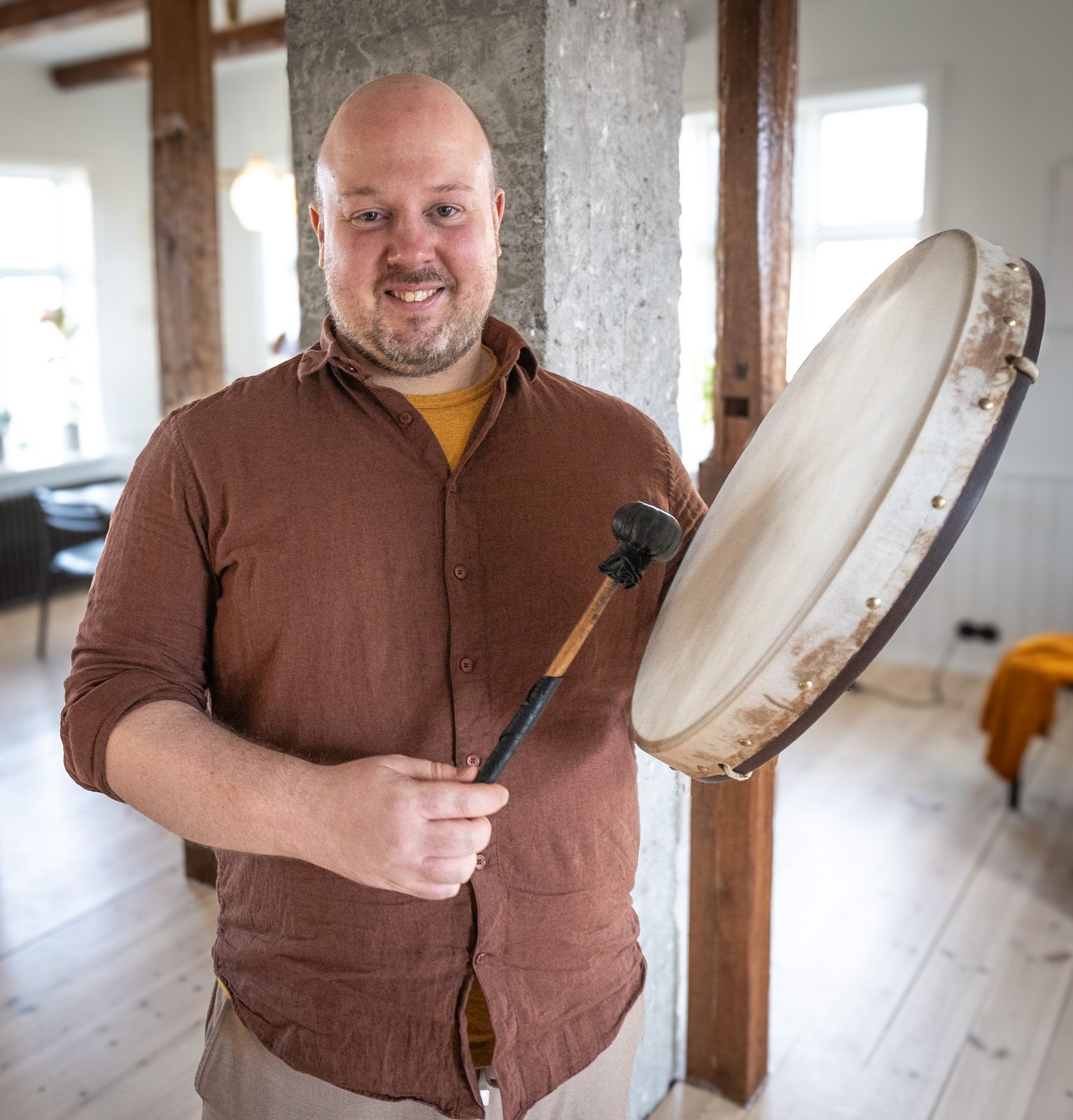 A man in a brown shirt is holding a drum and smiling
