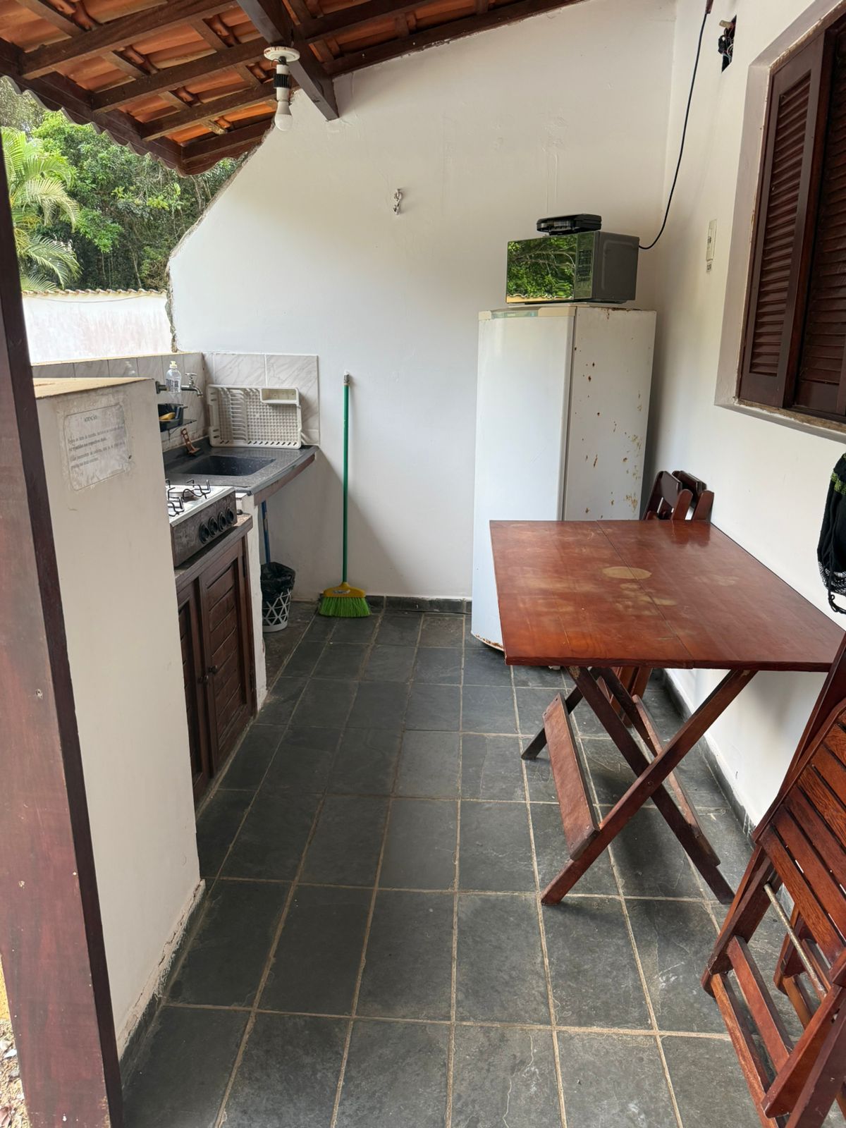 Cozinha externa com mesa, geladeira e fogão. Telhado e piso de telha marrom.