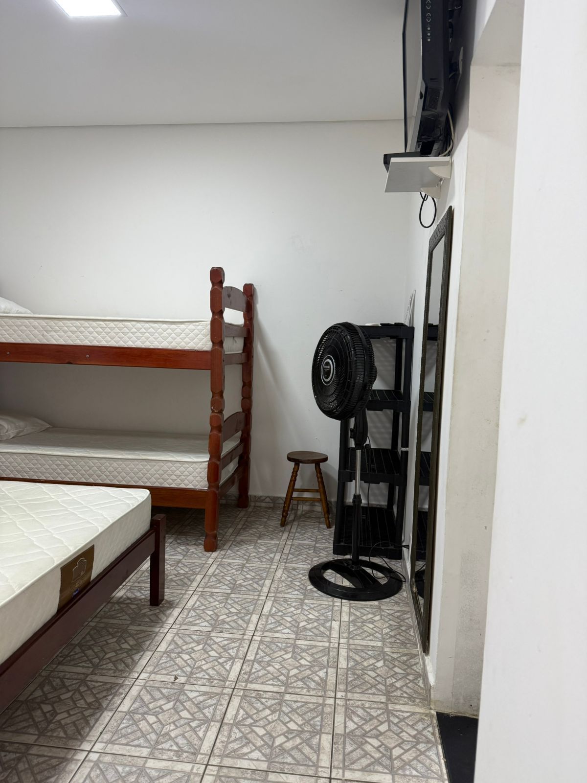Beliches e uma cama de solteiro em um quarto. Ventilador, banquinho e espelho também estão disponíveis.