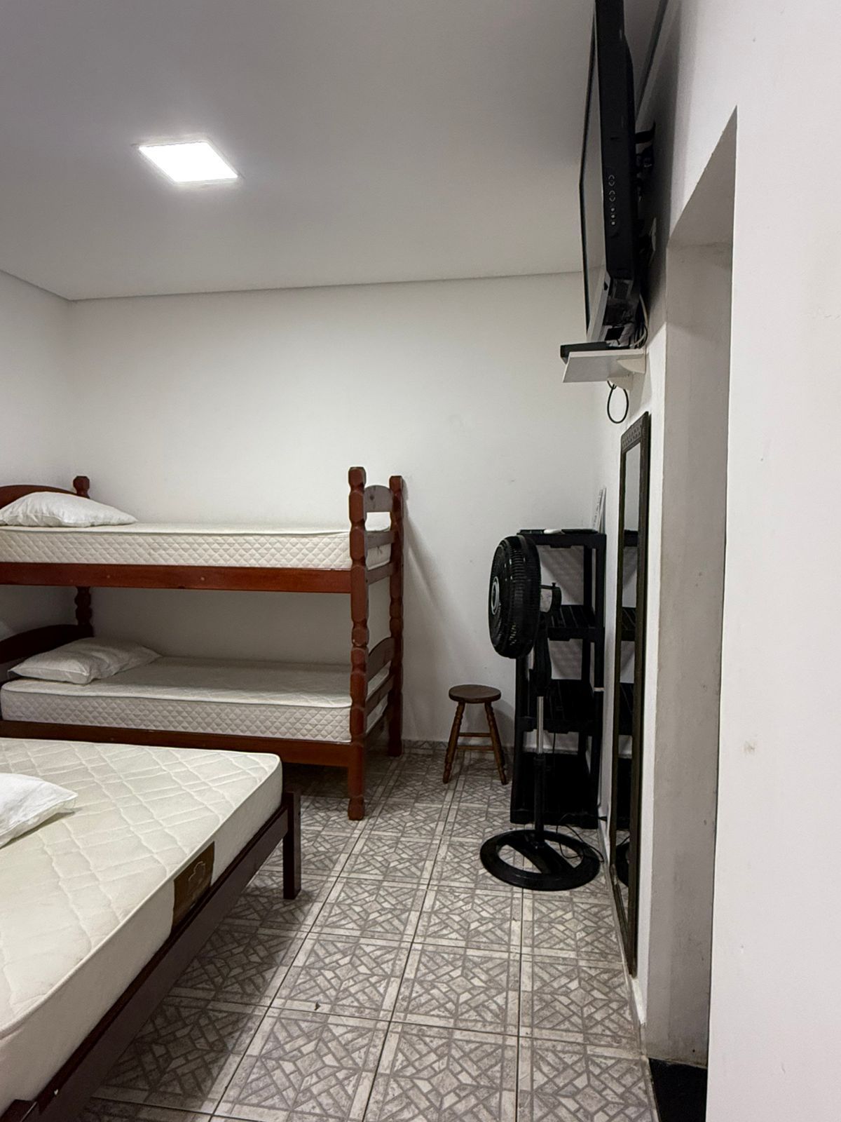 Um dormitório com beliches, uma cama de solteiro, um ventilador e uma TV na parede.