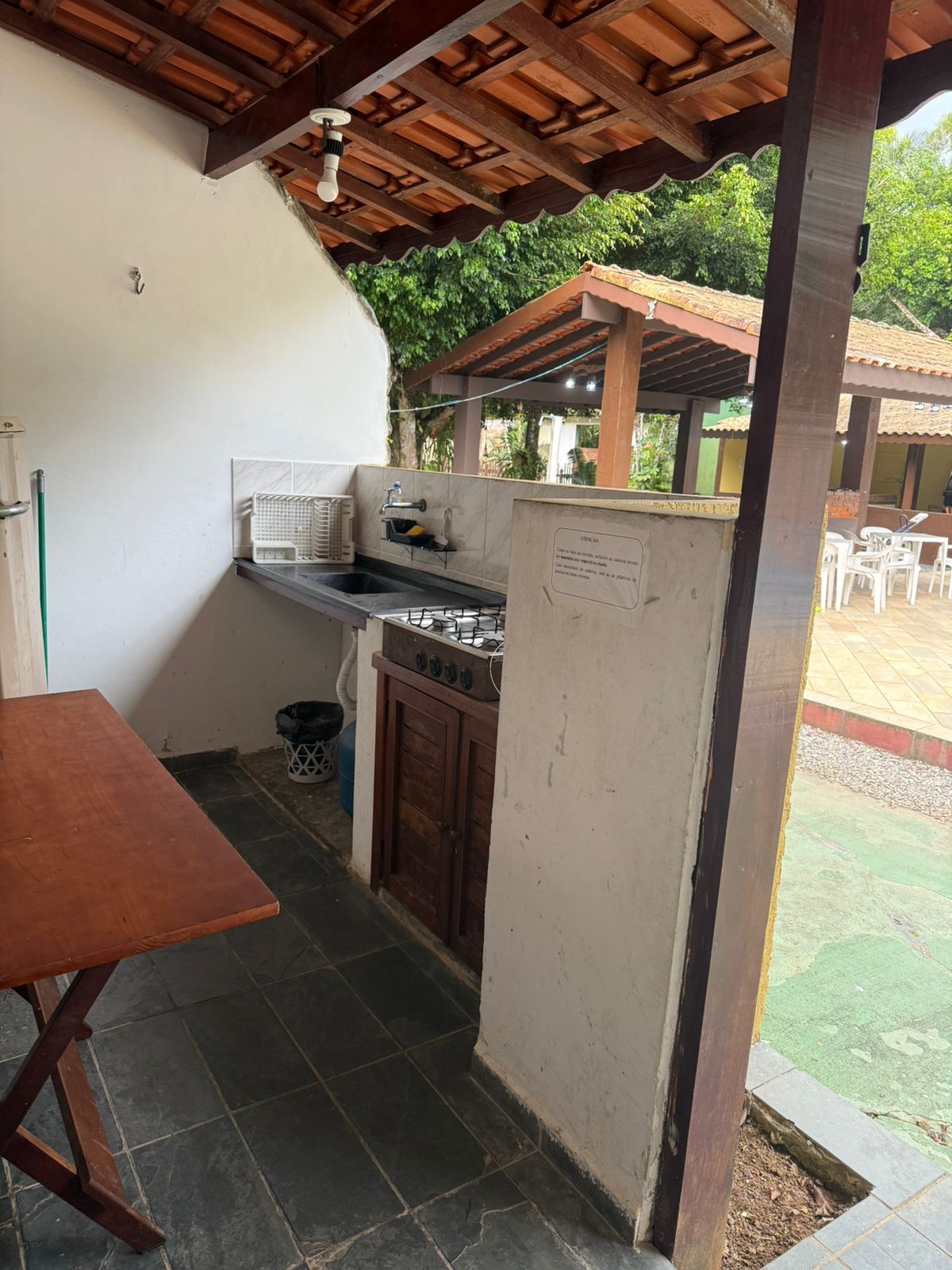 Cozinha ao ar livre com fogão, pia e mesa de jantar, sob um telhado de madeira.