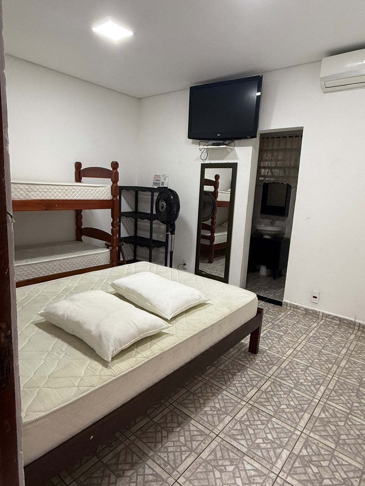 Quarto com beliche, cama queen size, TV, espelho e acesso ao banheiro.