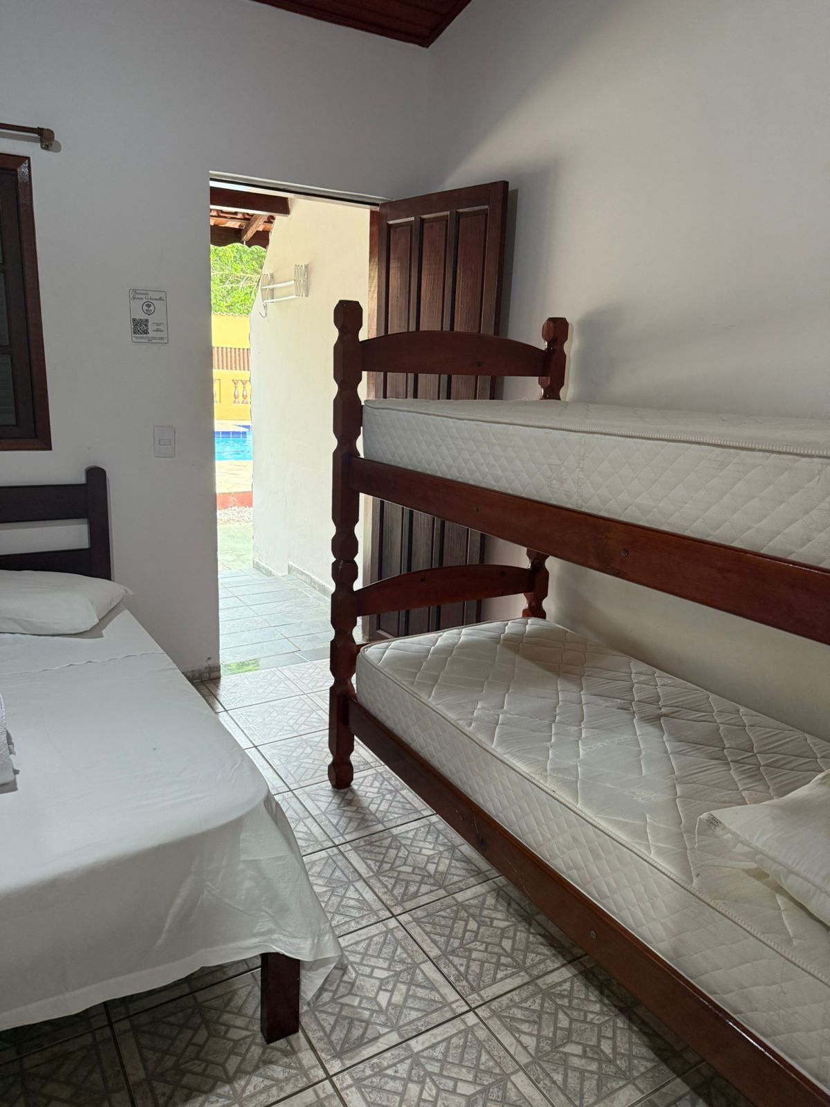 Quarto com beliche, cama de solteiro, porta aberta que leva à área da piscina.