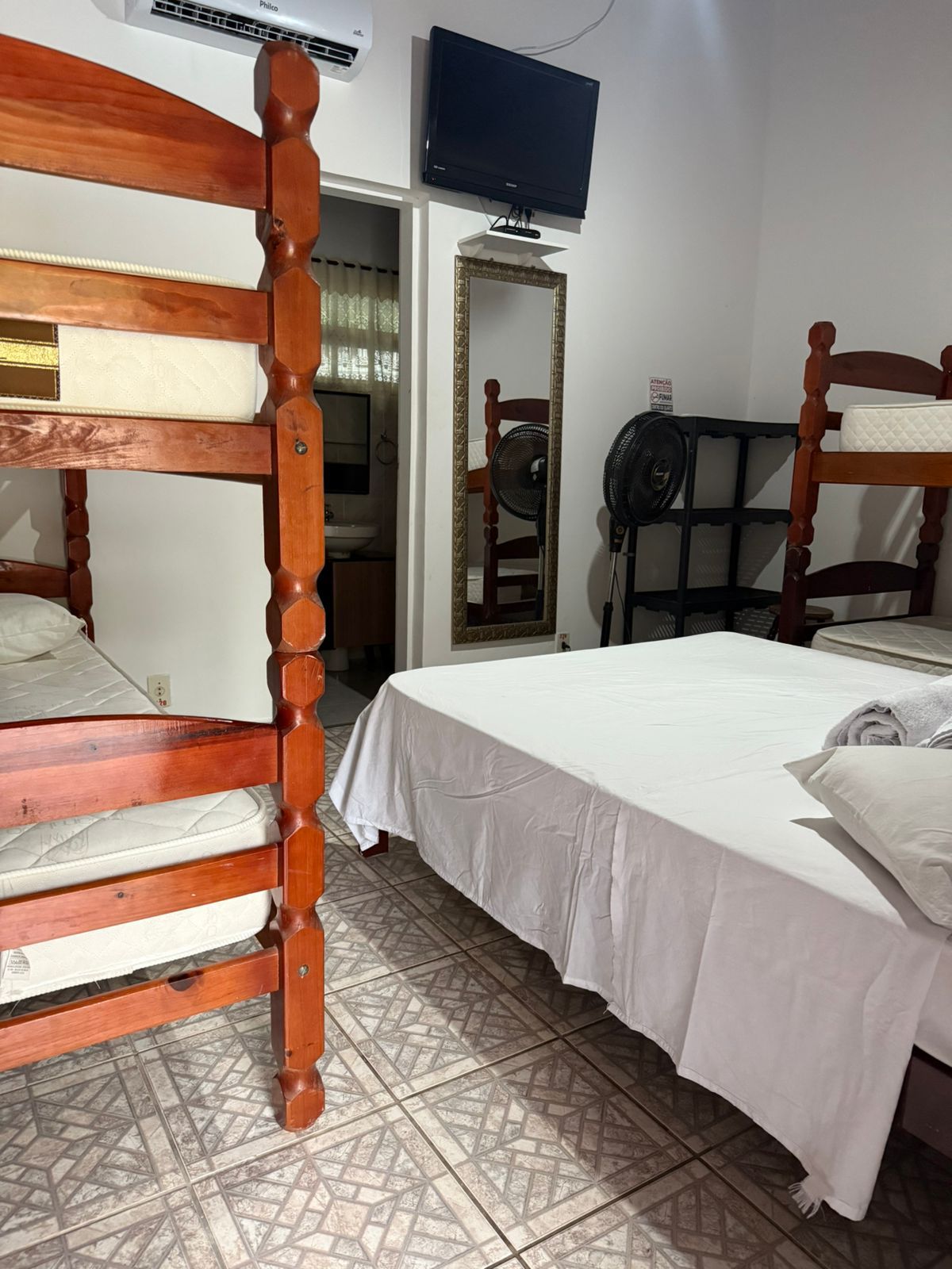 Beliches e uma cama de casal em um quarto pequeno, com espelho e TV na parede.