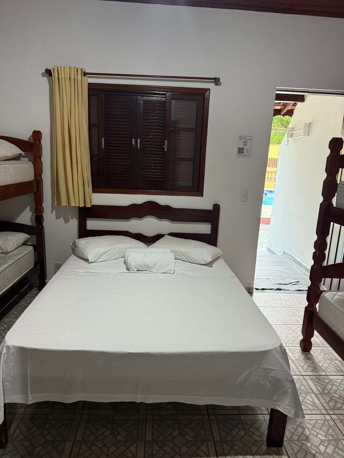 Quarto com cama, beliches, janela e porta para o exterior.