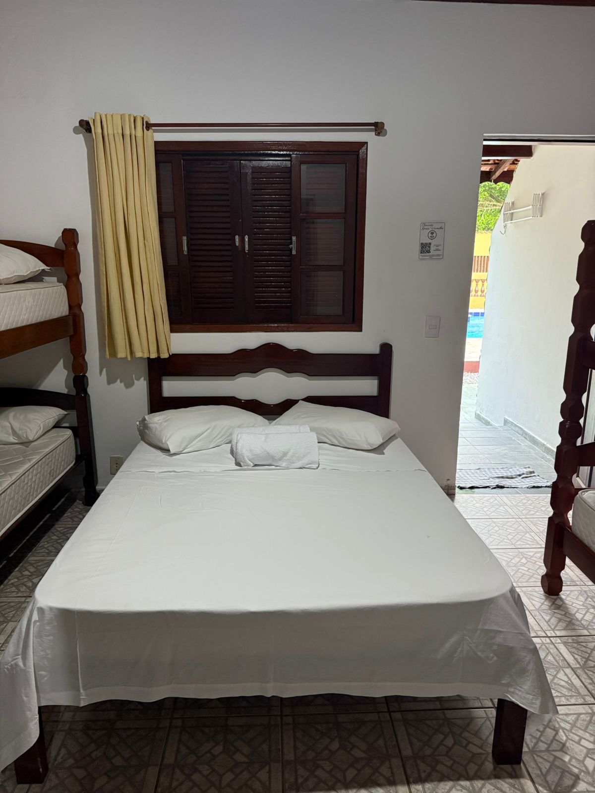 Quarto com uma cama de casal, dois beliches e uma janela com vista para a piscina.