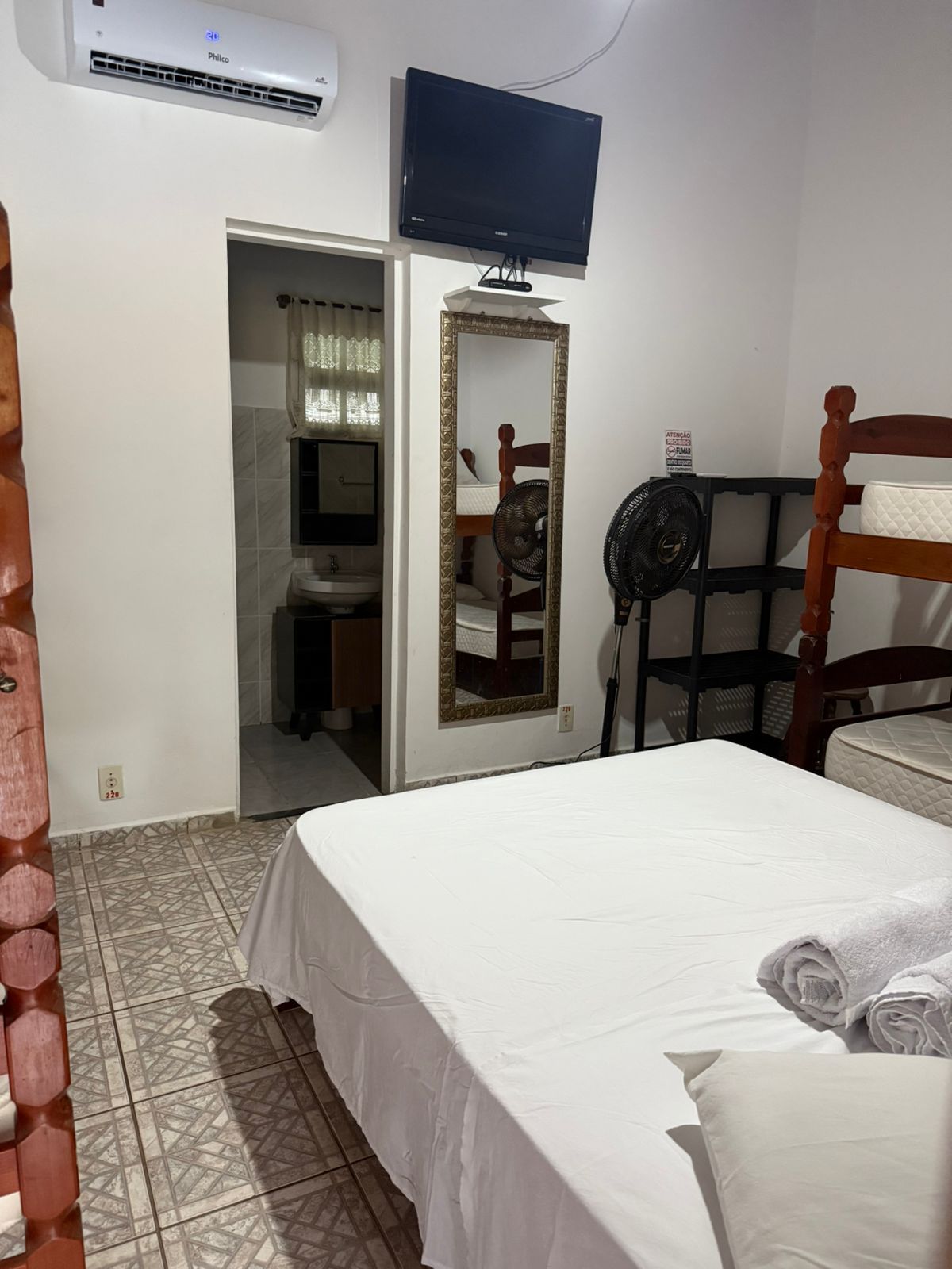 Quarto com cama, televisão, espelho e acesso ao banheiro.