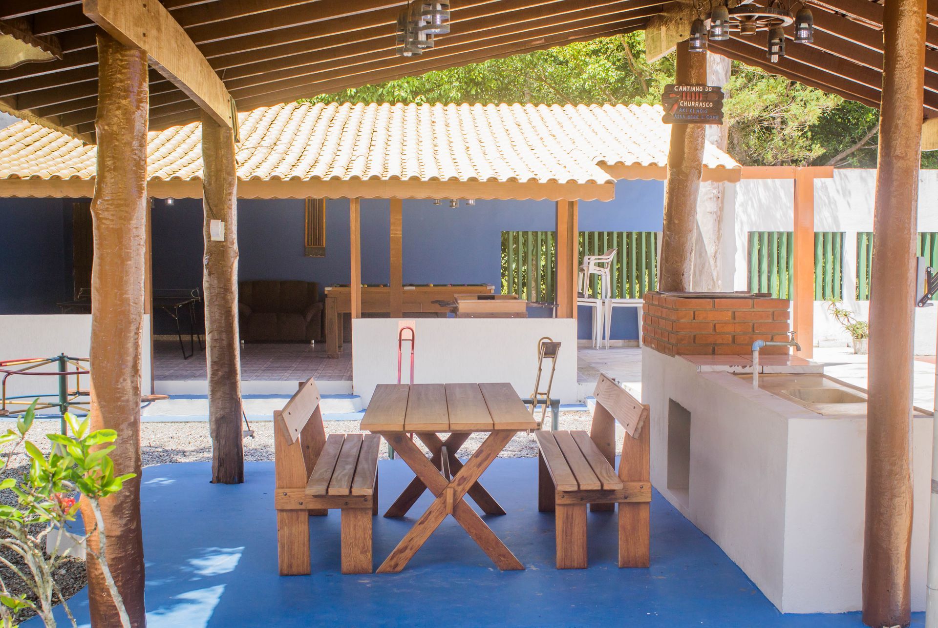 Pátio externo com móveis de madeira, piso azul e área de cozinha.