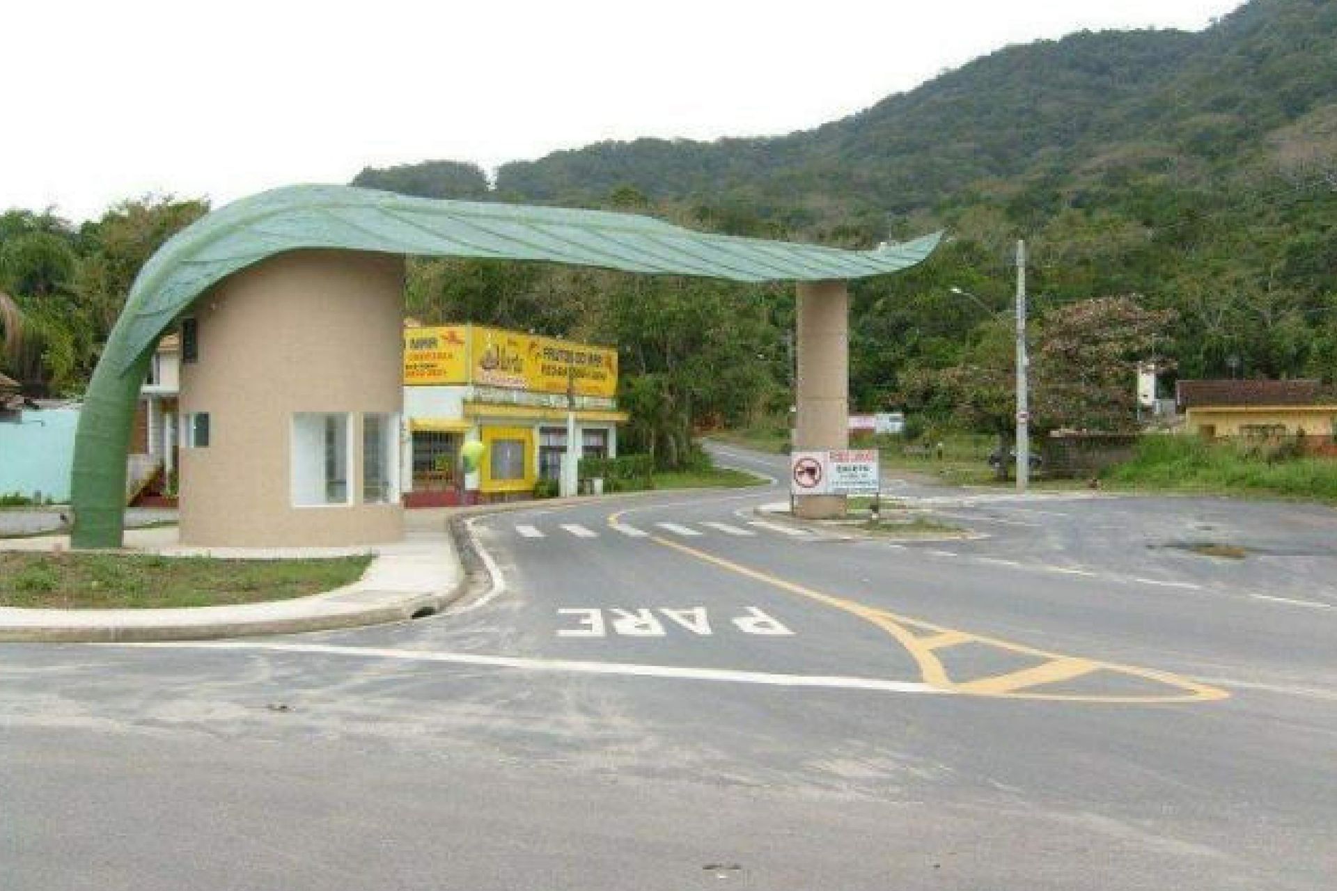 Portão com telhado verde em forma de folha, estrutura bege, estrada com marcação 