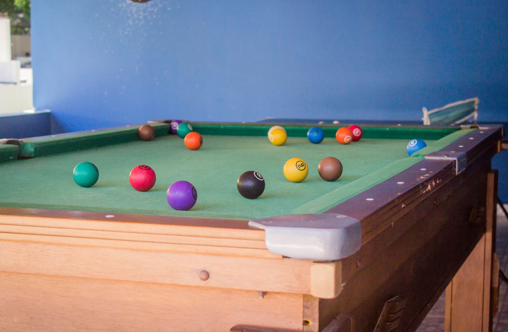 Mesa de sinuca com bolas de bilhar coloridas sobre uma superfície de feltro verde; uma parede azul ao fundo.