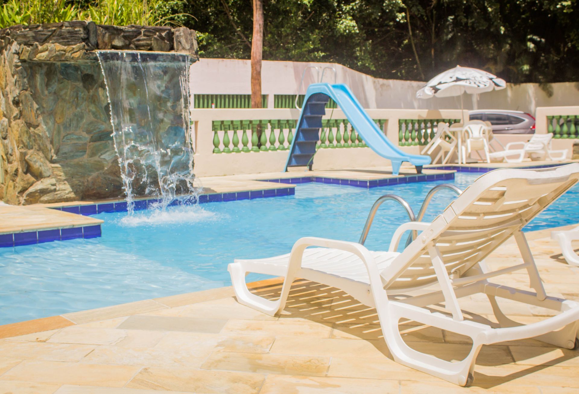 Piscina com cascata, toboágua azul, espreguiçadeiras e guarda-sol.