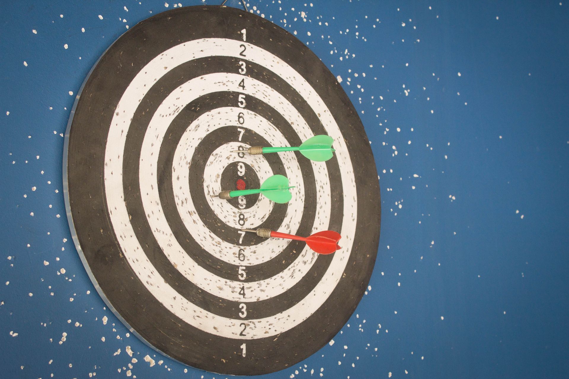 Alvo de dardos com três dardos: dois verdes no centro do alvo e um vermelho na seção 8. Fundo de parede azul.