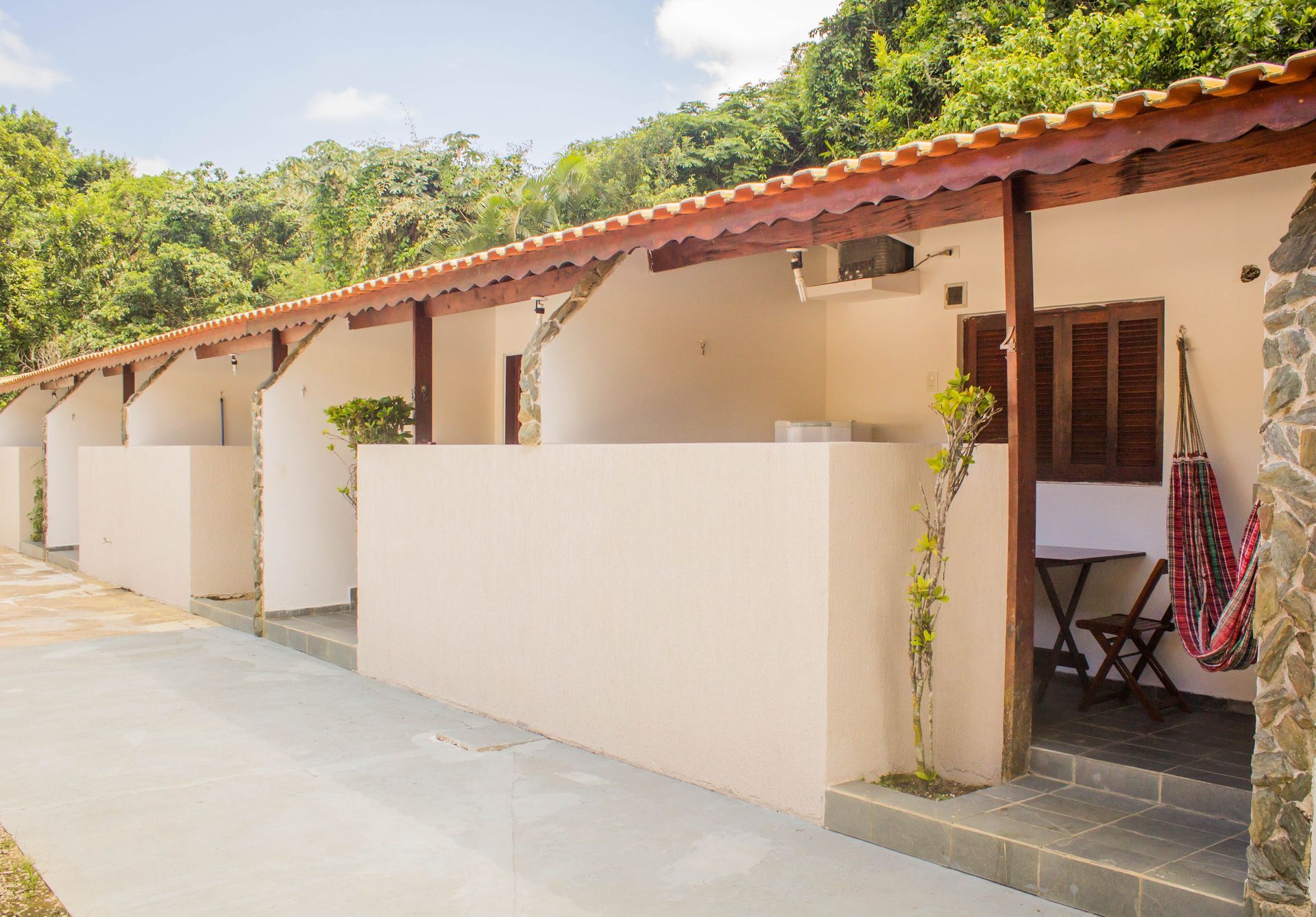 Fileira de cabanas bege com telhados vermelhos, vigas de madeira e pátios privativos; situadas em uma paisagem verdejante.