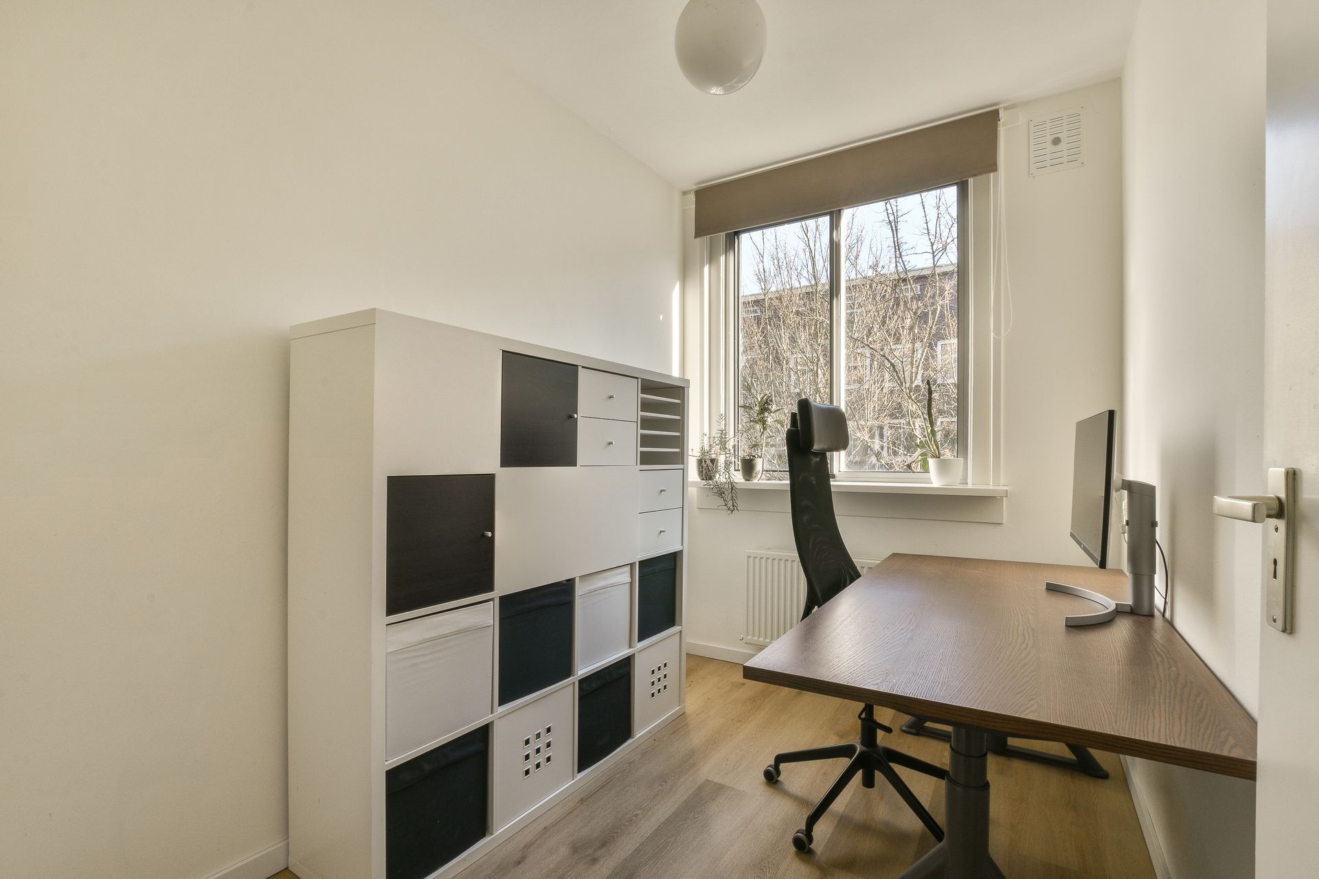 Home office with a dark desk, black chair, and storage cabinet under a window.