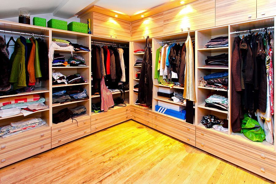 Walk-in closet with light wood cabinetry and shelves filled with clothing, shoes, and accessories.