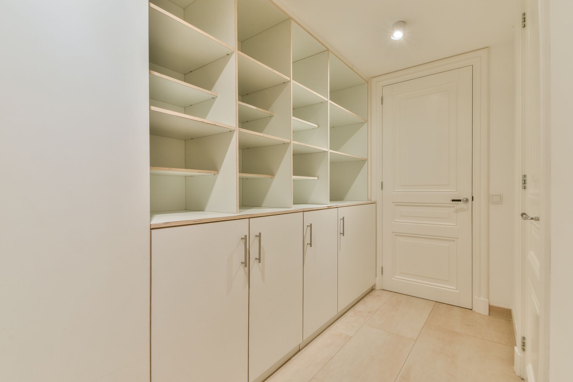 White built-in storage cabinets with shelves and doors in a hallway, next to a white door.