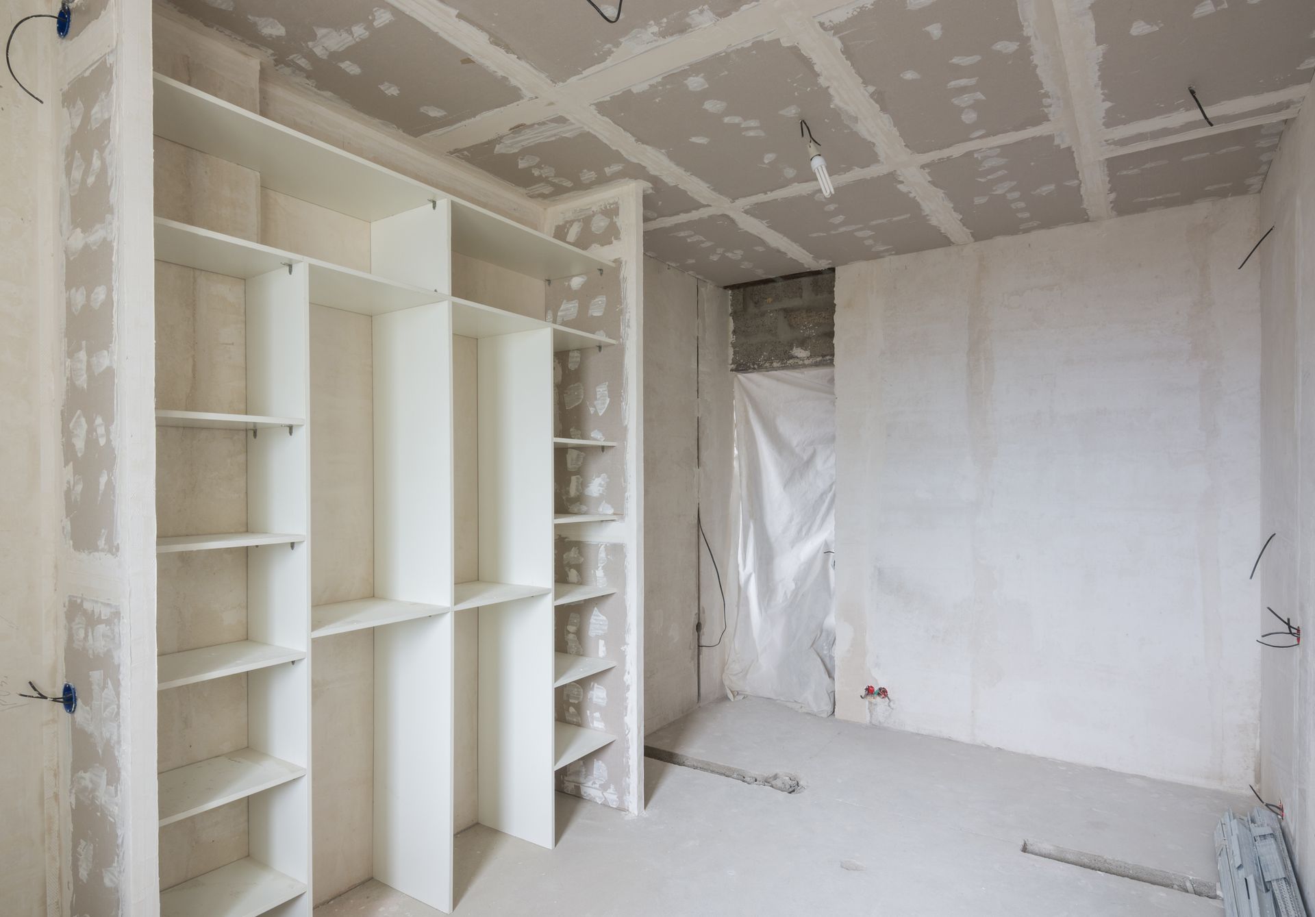Interior room under construction, with white shelving unit, drywall, and unfinished ceiling.