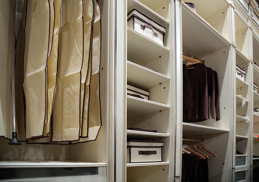 White closet with shelves, hanging clothes, and storage boxes.