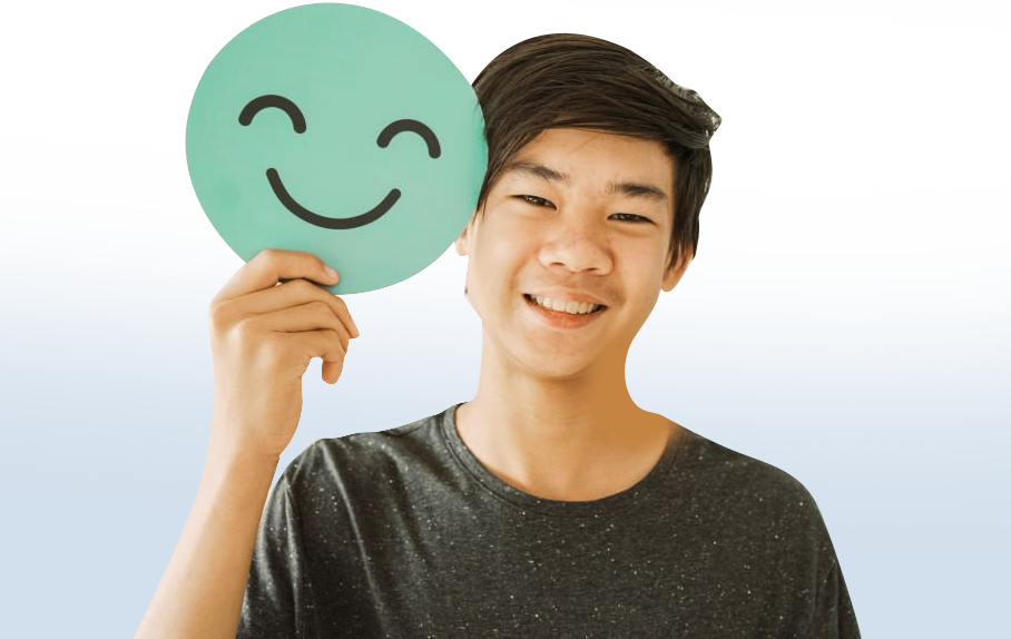 A young man is holding a smiley face in front of his face.