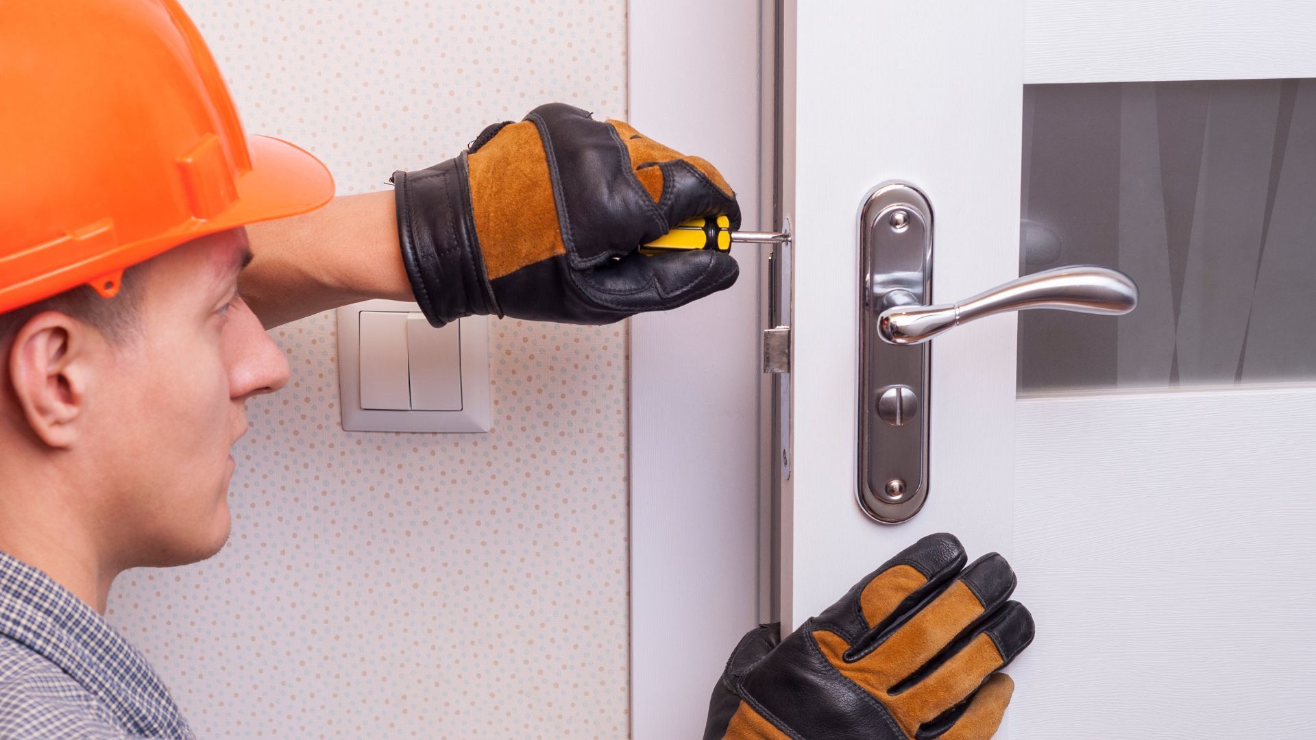 Worker in orange hard hat and gloves adjusting a door handle on a white interior door