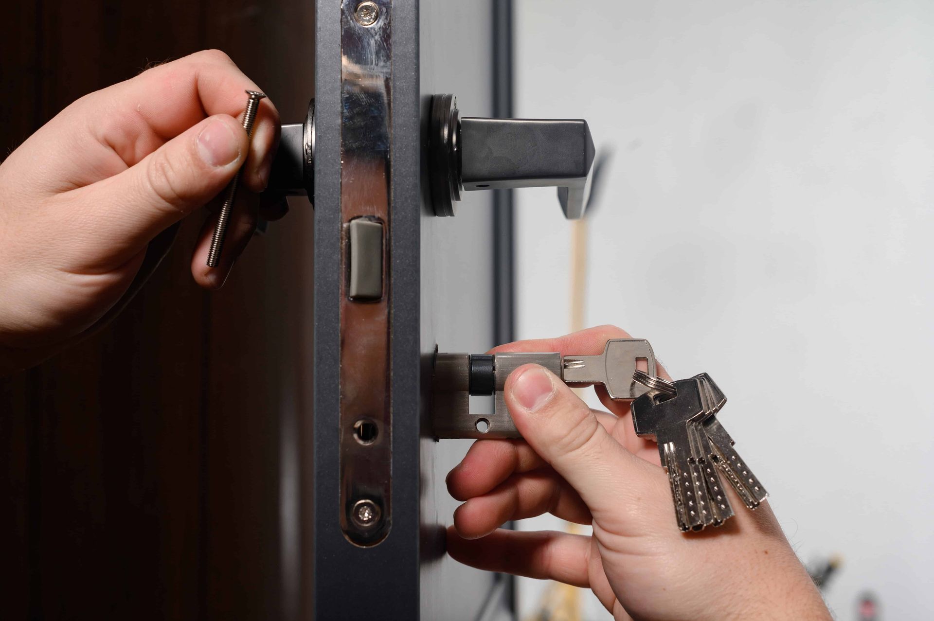 Hands use a key to unlock a door latch and handle.