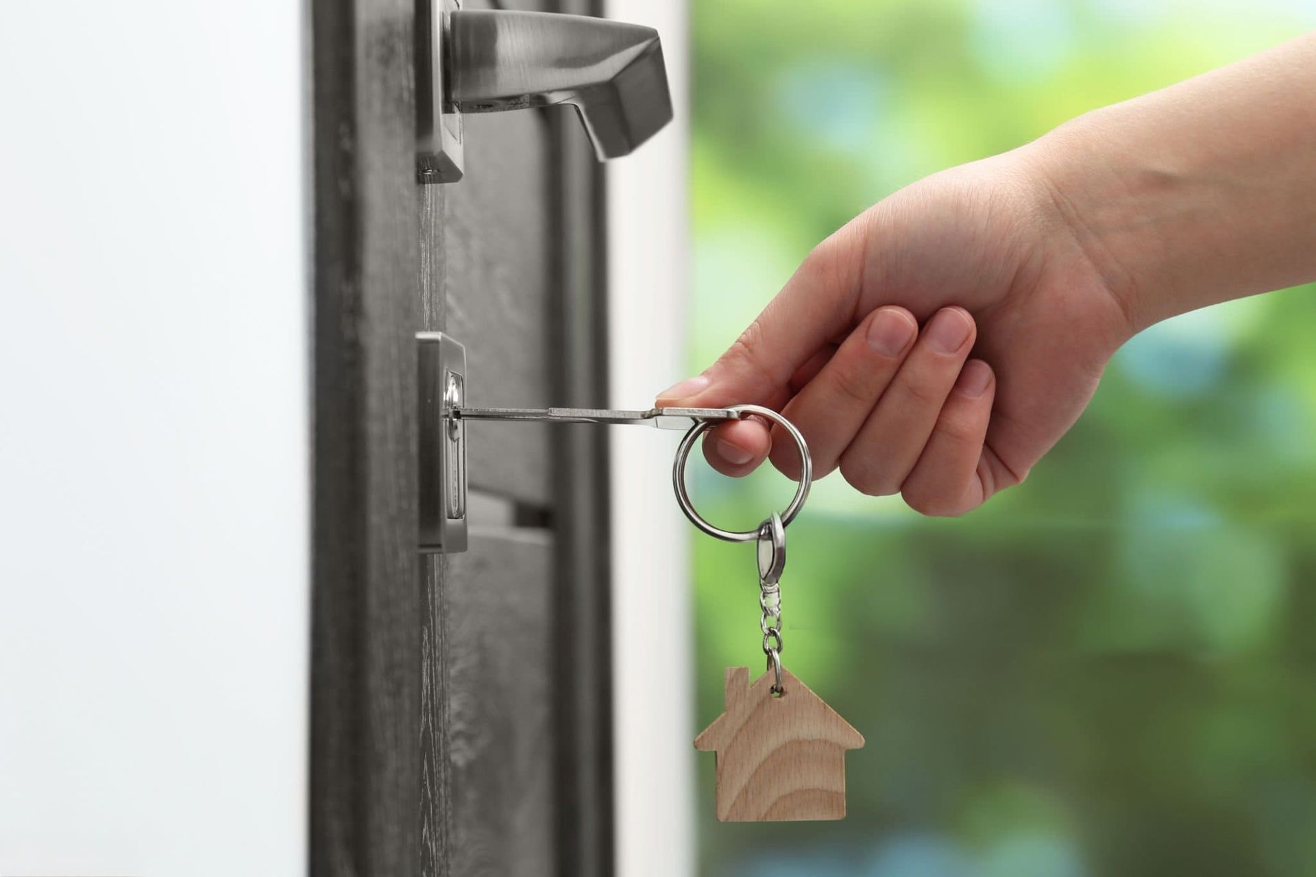 Hand inserting a key into a door lock with a house-shaped keychain