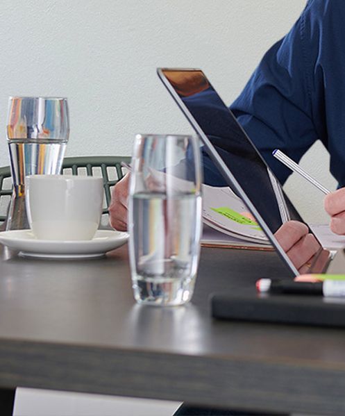Een persoon zit aan een tafel met een kopje koffie en een glas water
