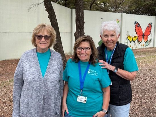 Three women are posing for a picture in front of a wall with butterflies on it