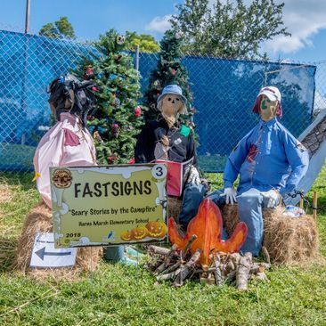 A group of scarecrows are sitting on hay bales in front of a christmas tree.