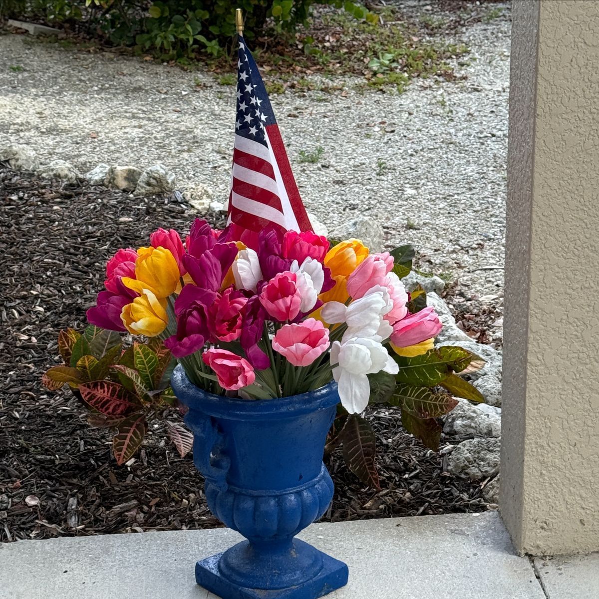 A blue vase filled with flowers and an american flag