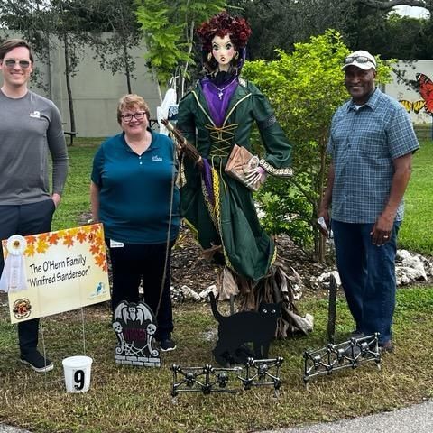 A group of people are standing in front of a scarecrow.