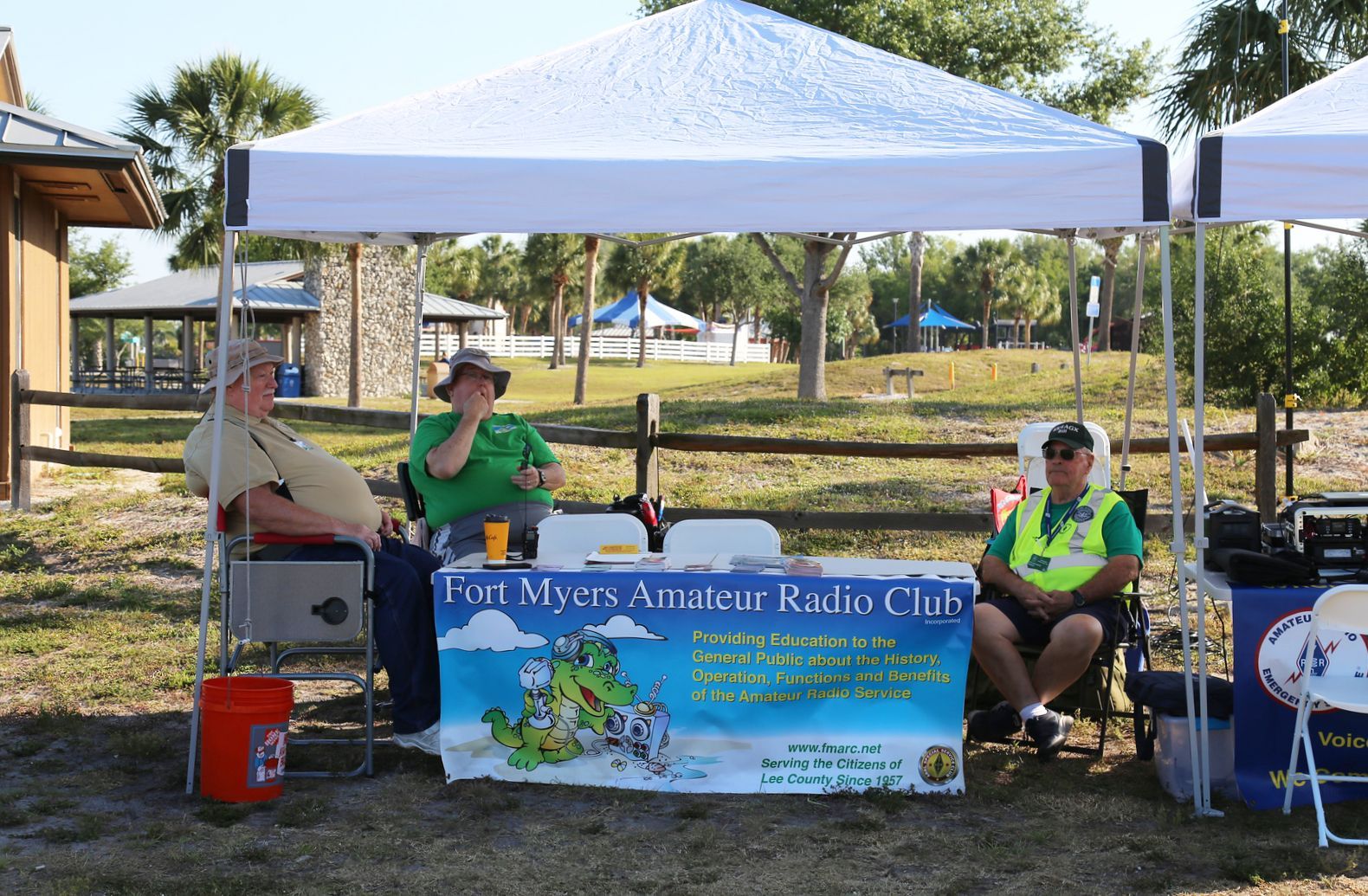 Two men sit at a table under a tent that says amateur radio club
