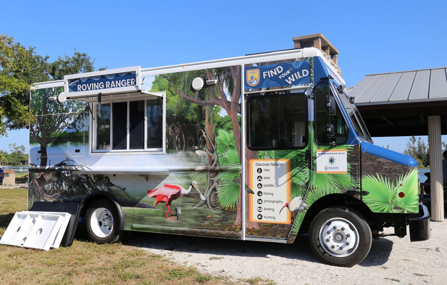 A food truck with a bird on the side is parked in a field.