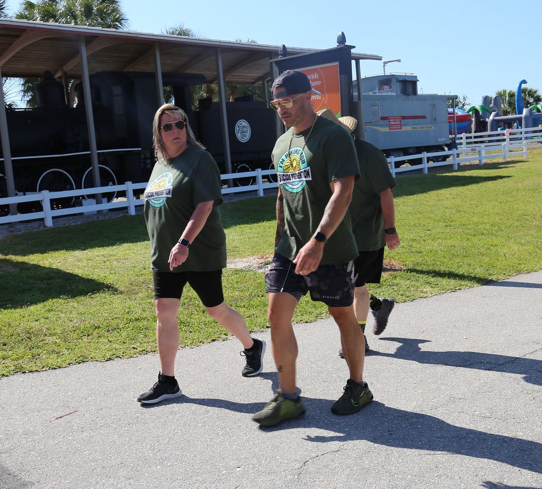 A group of people are walking down a sidewalk in front of a train