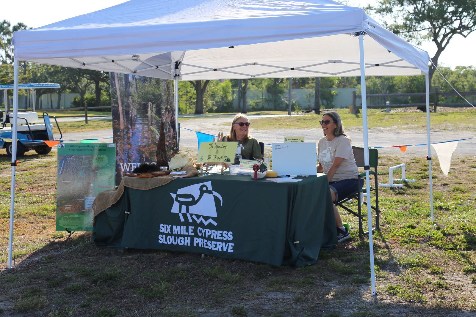 Two women are sitting at a table under a tent.