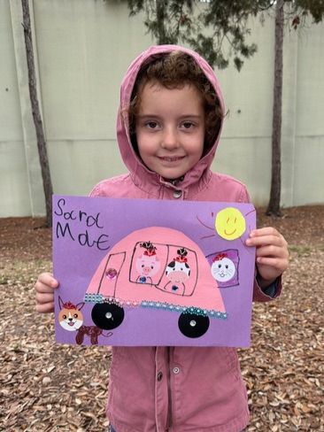 A little girl is holding a drawing of a pink bus.