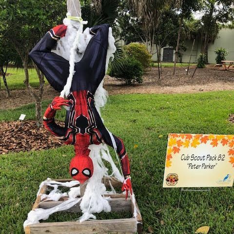 A scarecrow dressed as spider-man is hanging upside down on a wooden crate.