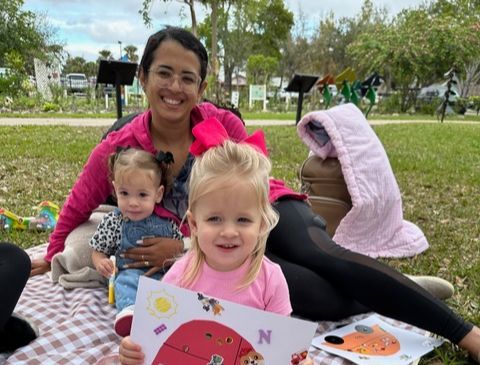 A woman is laying on a picnic blanket with two little girls.