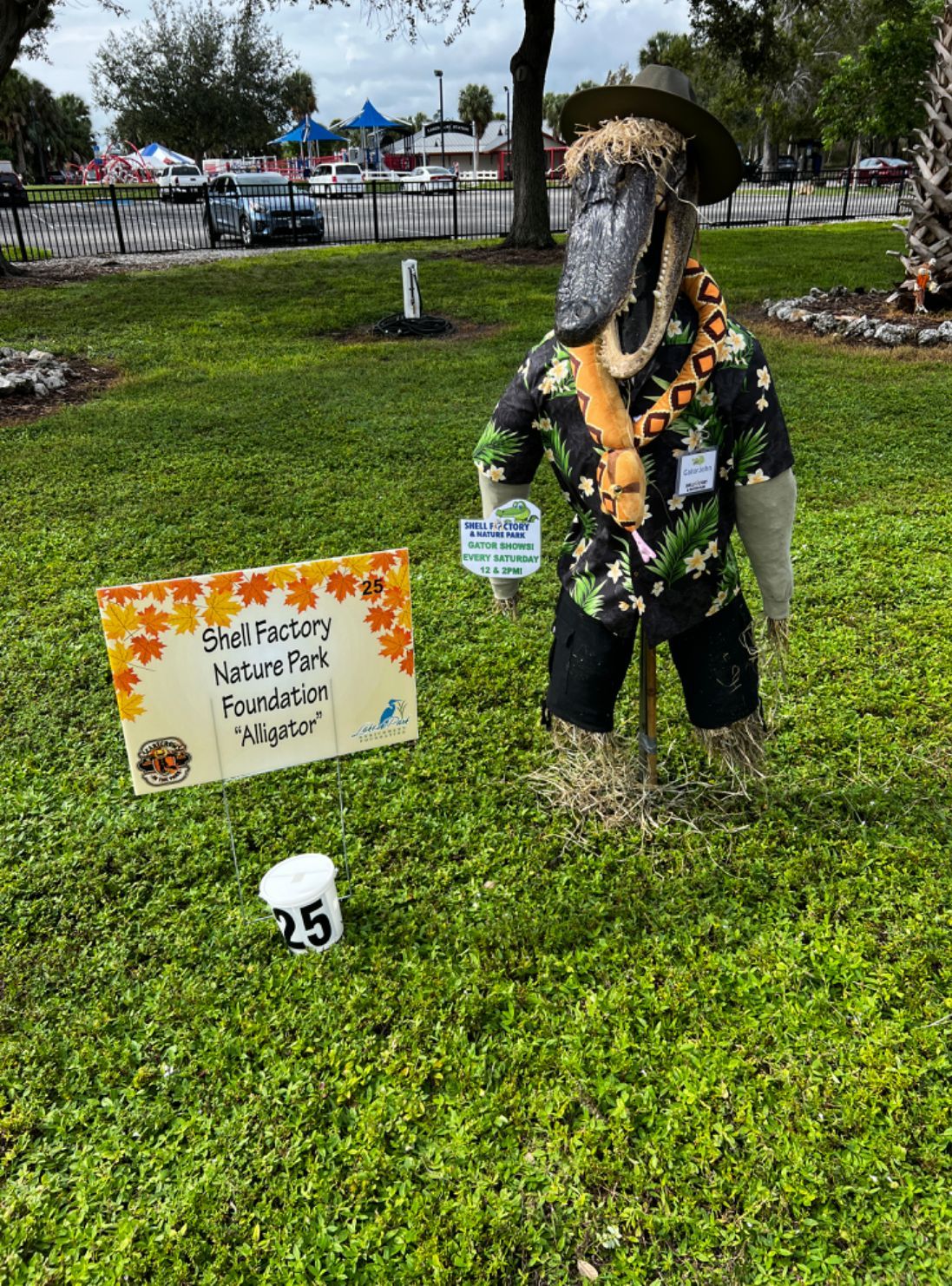 A scarecrow is standing in the grass next to a sign.
