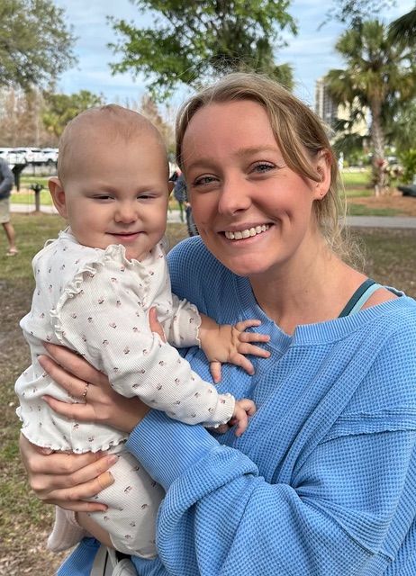 A woman in a blue sweater is holding a baby in her arms.