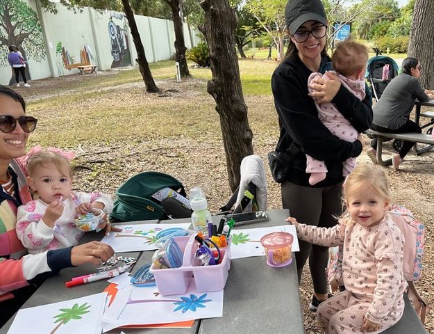 A woman is holding a baby while sitting at a table with other children.