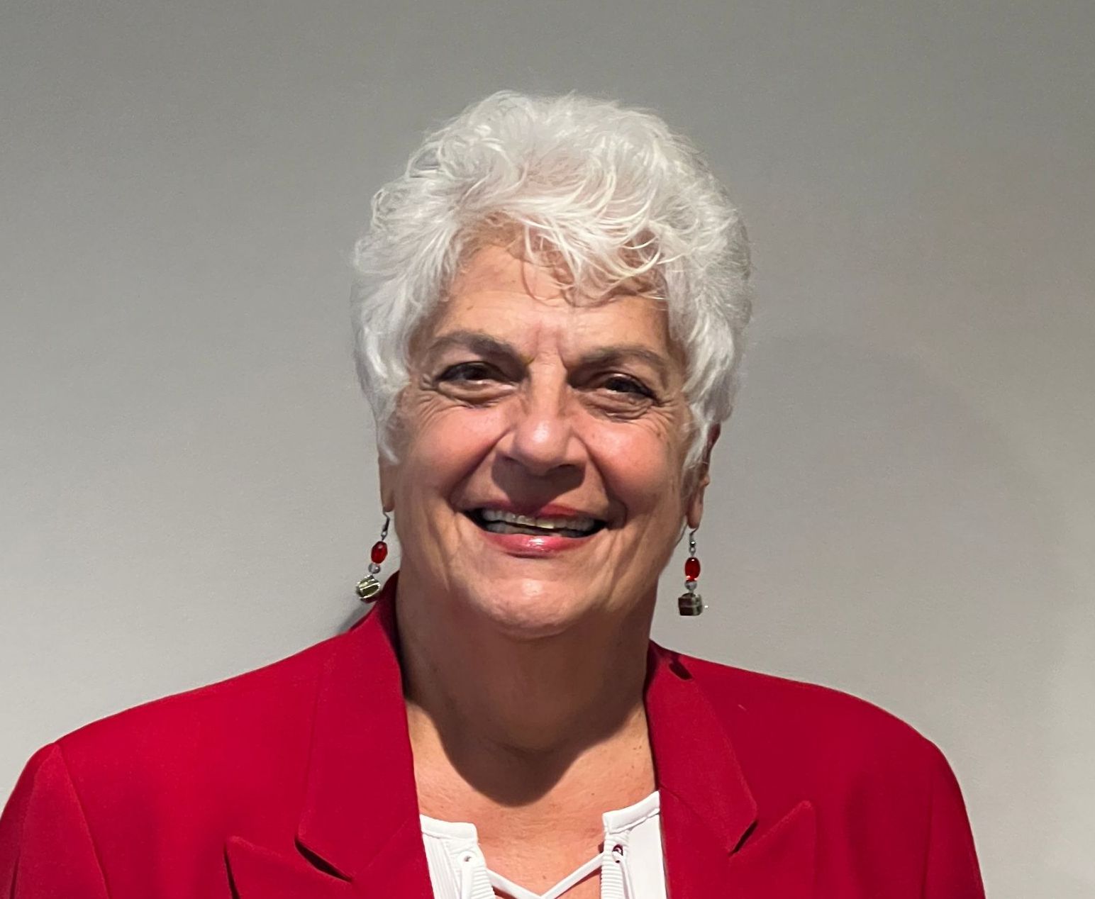 A woman with white hair is wearing a red jacket and earrings.